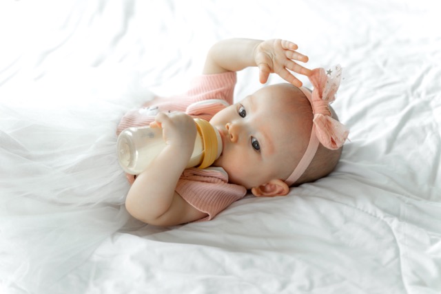 Babies drink milk from a bottle on white bed. Expert Strategies for Infant Feeding from Red Door Pediatric Therapy