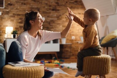 Cheerful mother giving high-five to her small son at home. Your Journey Begins at Red Door Pediatric Therapy